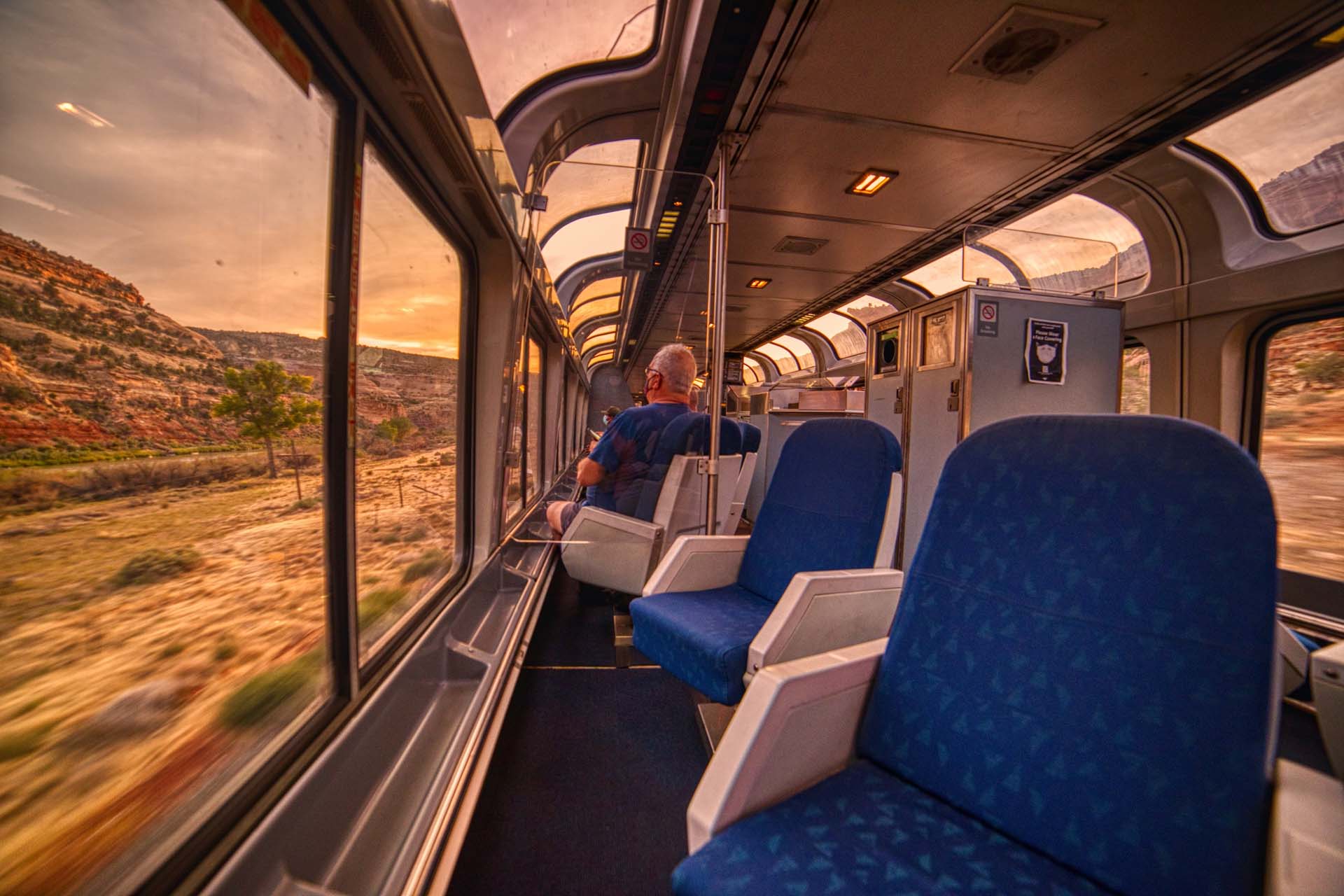 A passenger sitting in a lounge on a train with panoramic glass windows taking in desert views in Colorado, USA