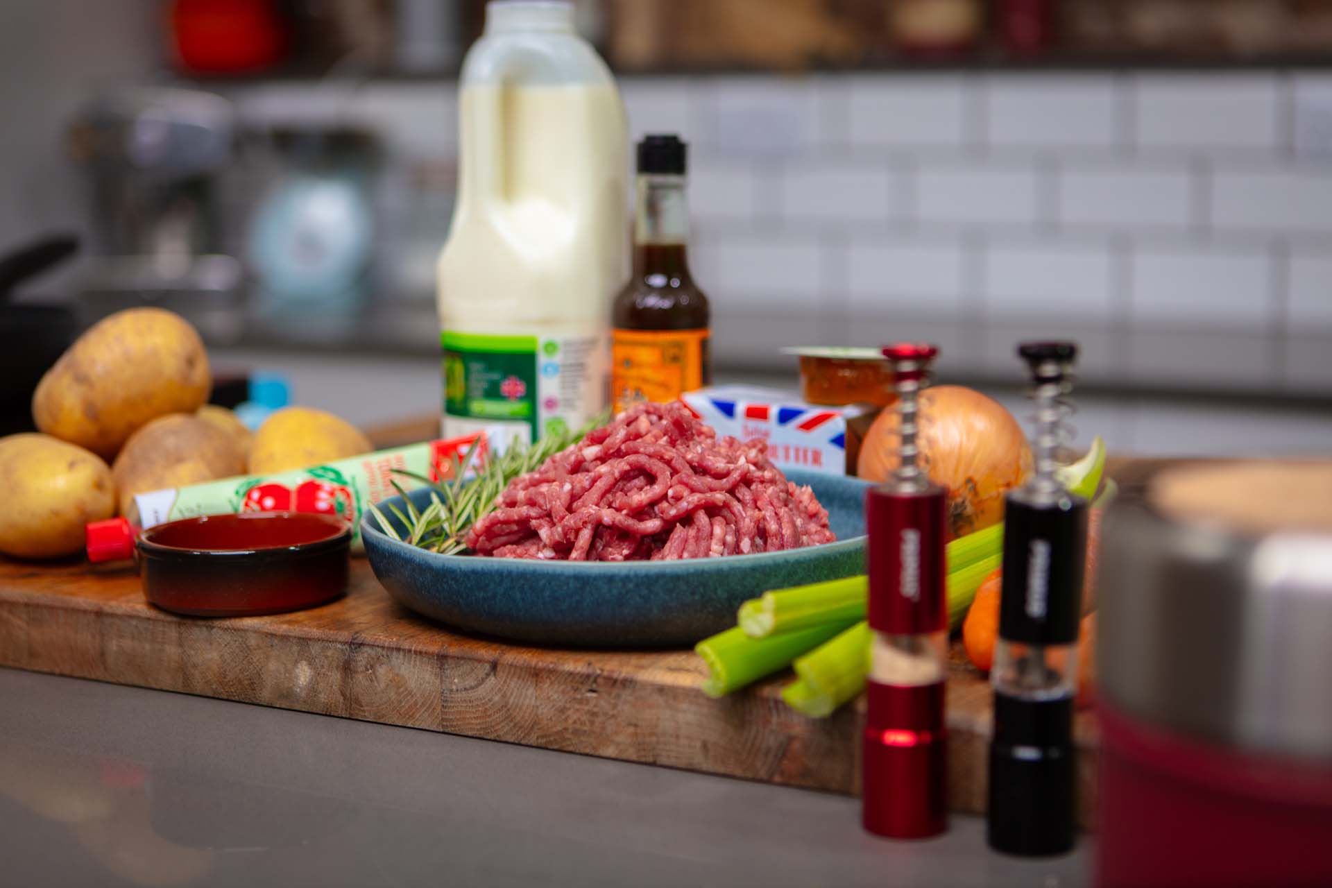 Ingredients for a shepherd's pie on a wooden worktop including mince, potatoes, celery, an onion, milk and carrots.