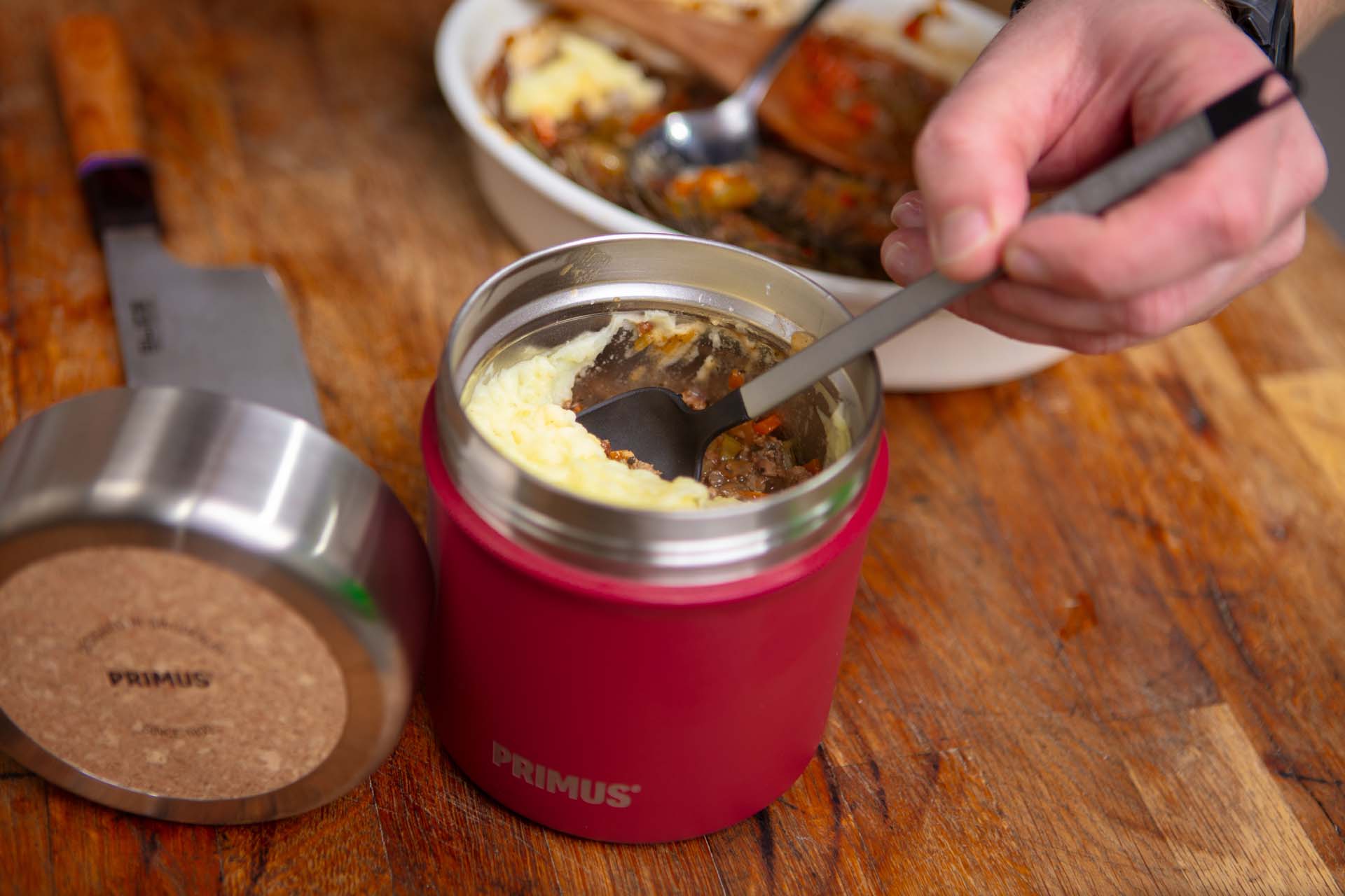 Someone putting a cooked shepherd's pie into a red flask to eat outdoors