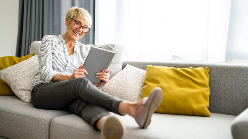 A senior woman sitting on the sofa smiling at a tablet