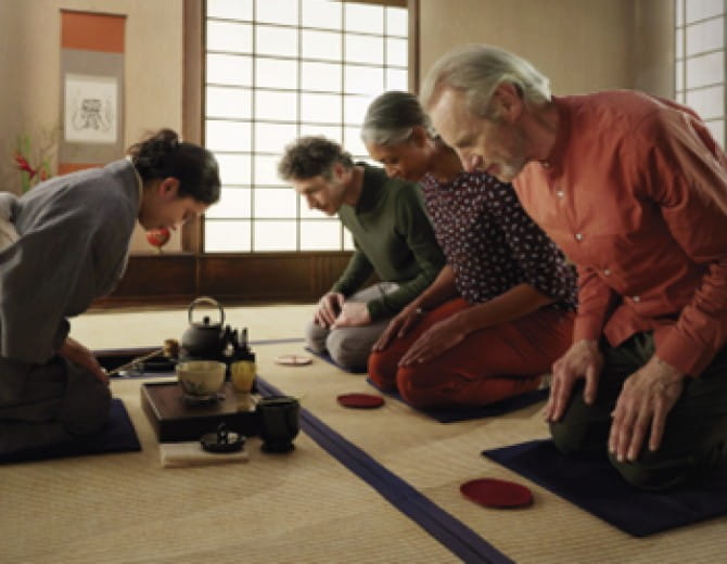 Group participating in a traditional Japanese tea ceremony, kneeling on tatami mats with tea set in front.