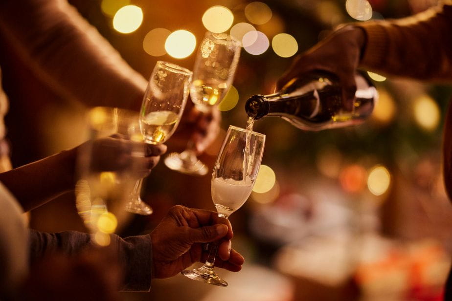 Champagne being poured into glasses during a festive celebration with warm, glowing lights in the background.