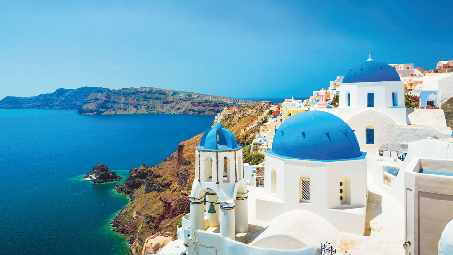 White buildings with blue domes overlooking the sea on a sunny Greek island