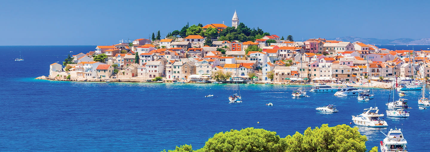 Colourful coastal town on a peninsula surrounded by blue sea, with boats moored in the harbour.
