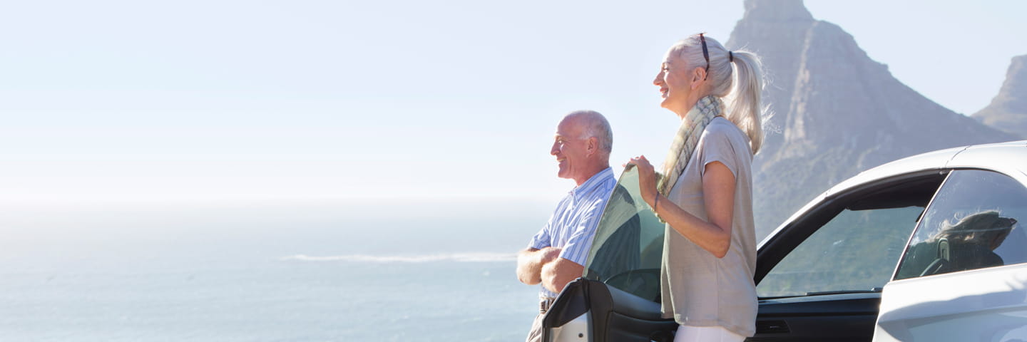 Two people standing next to a car gazing out at the sea