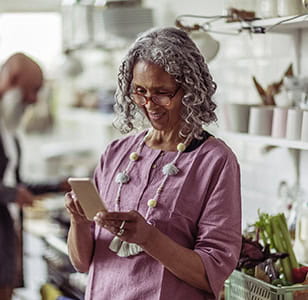 Mature woman in eyeglasses using smart phone in domestic kitchen