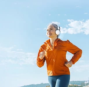 Mature woman listening to music through headphones and jogging on sunny day