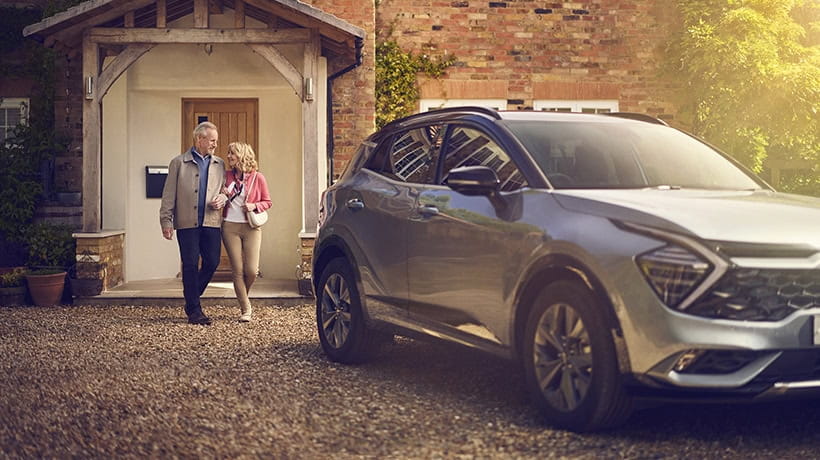 A mature couple walking arm in arm to their car parked on the driveway of their home