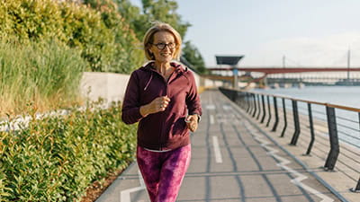 A mature woman running along a promenade on a sunny day.