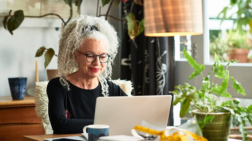 Grey haired woman at home smiling in front of laptop