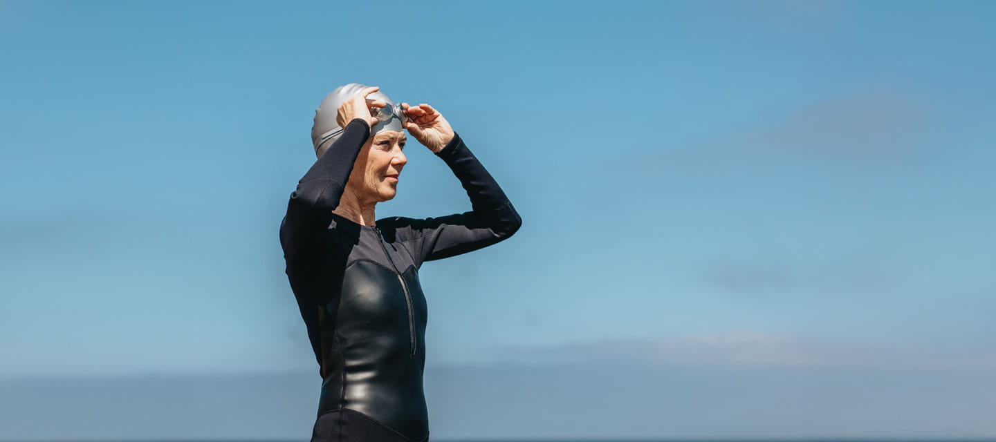 A lady in a black swimsuit putting her swimming googles on.