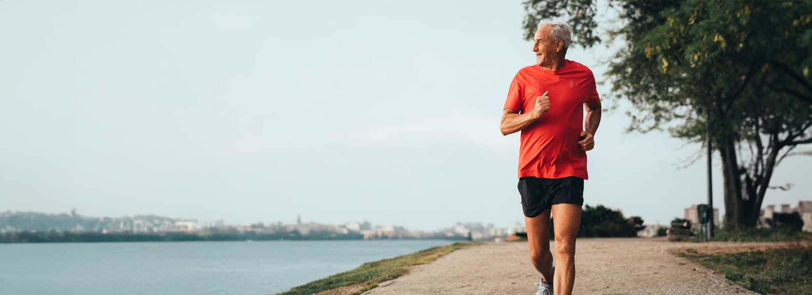 A man in a red running top running on a footpath by a river