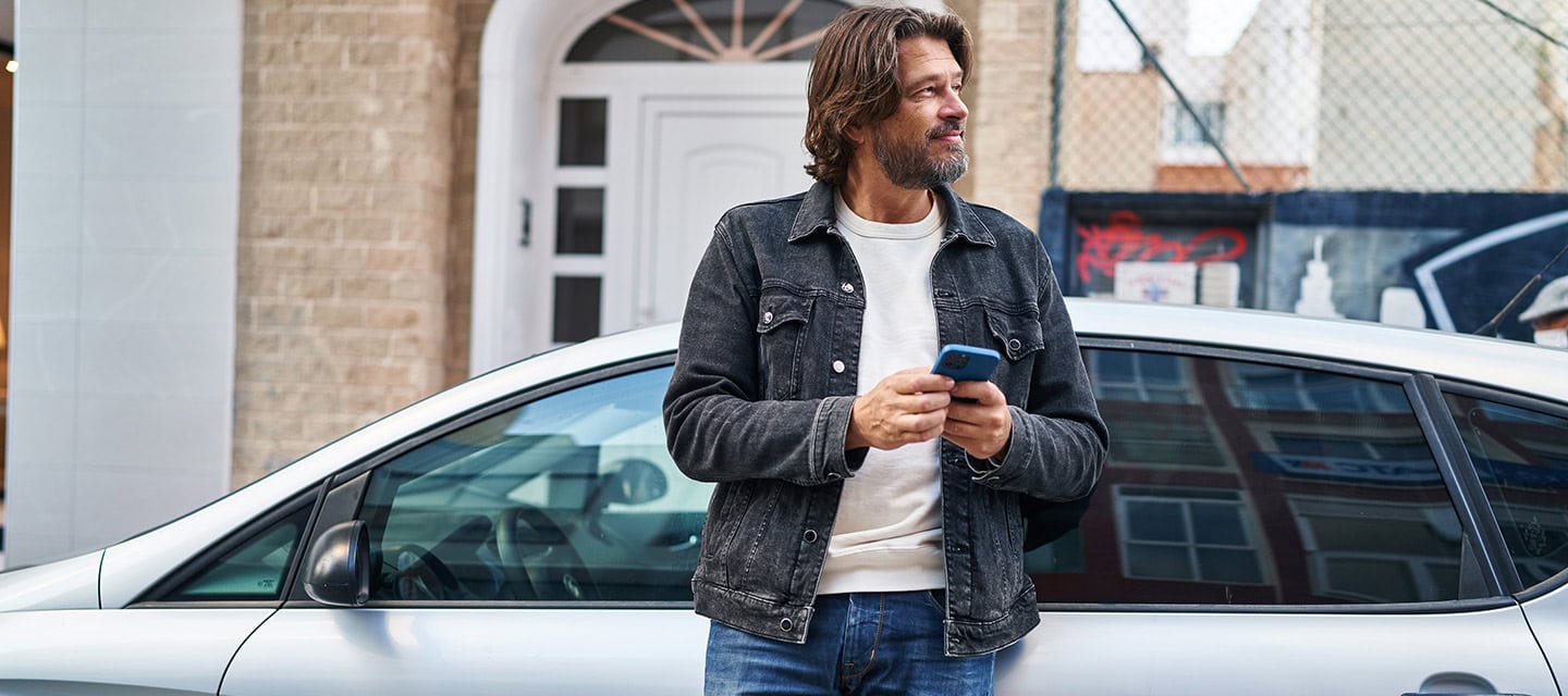 Middle age man using smartphone leaning on car at street