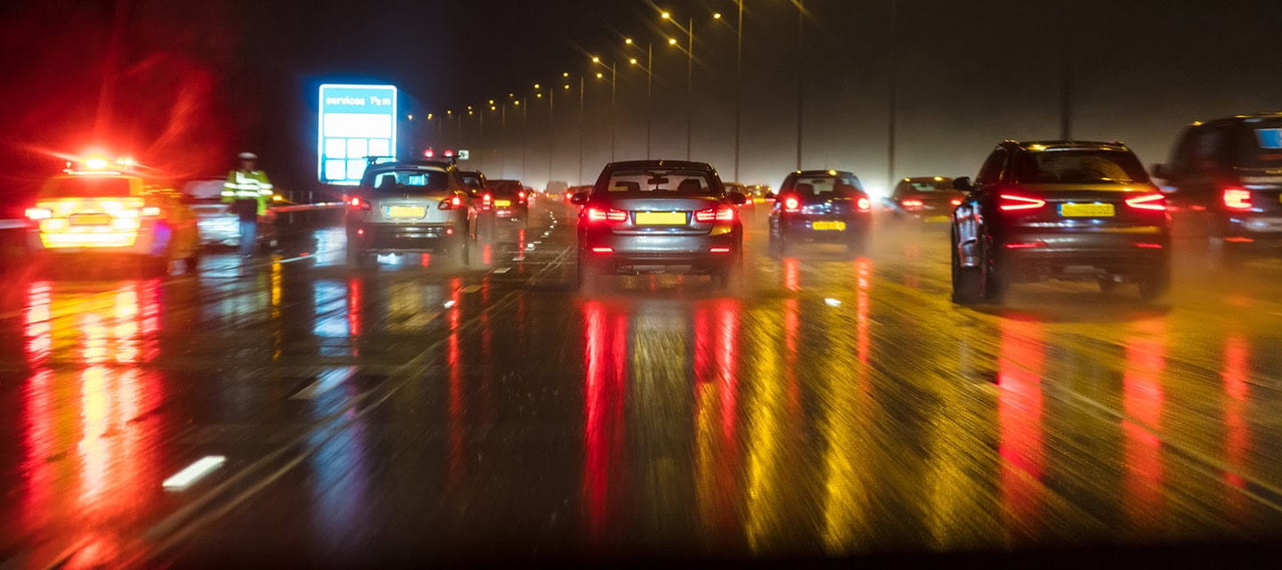Motion blurred photograph of traffic at in night in the rain on a British motorway with police officer and car.