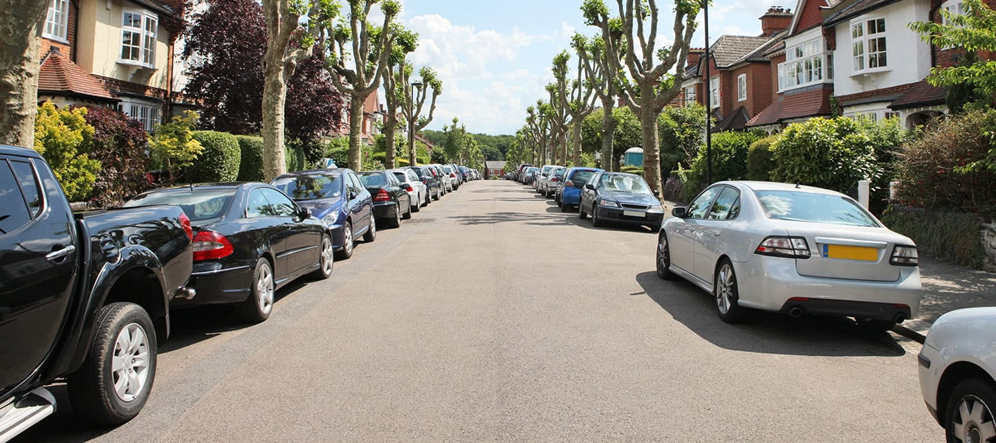 Tree lined UK Street with cars parked on either side.