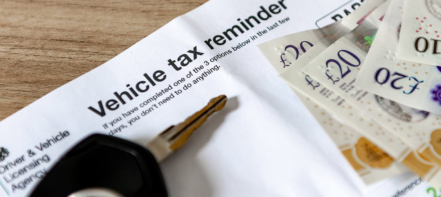 A vehicle tax reminder document of a desk with car keys and money.