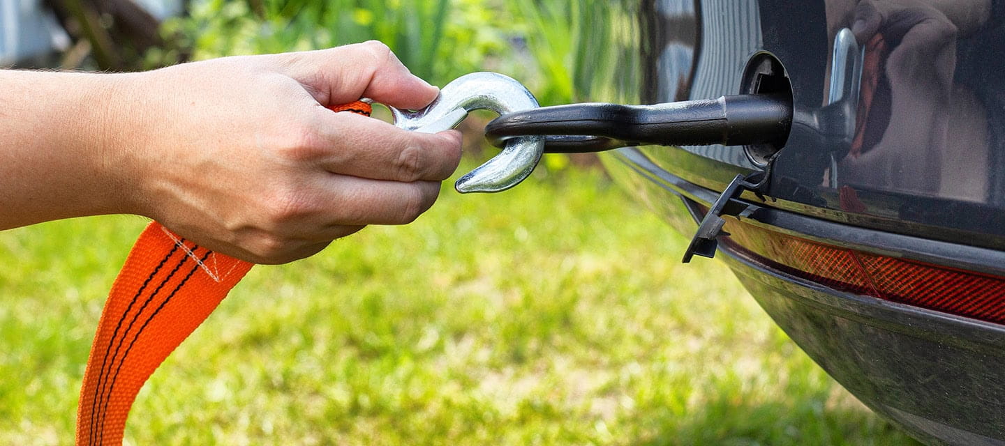 A hand attaching a car tow hook with an orange tow rope for towing.