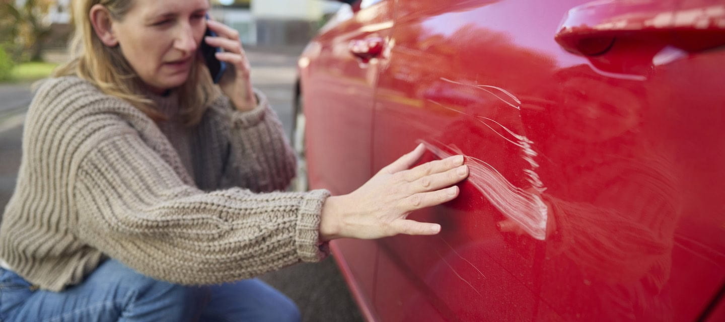 Unhappy mature female driver with damaged car after accident calling insurance company on mobile phone