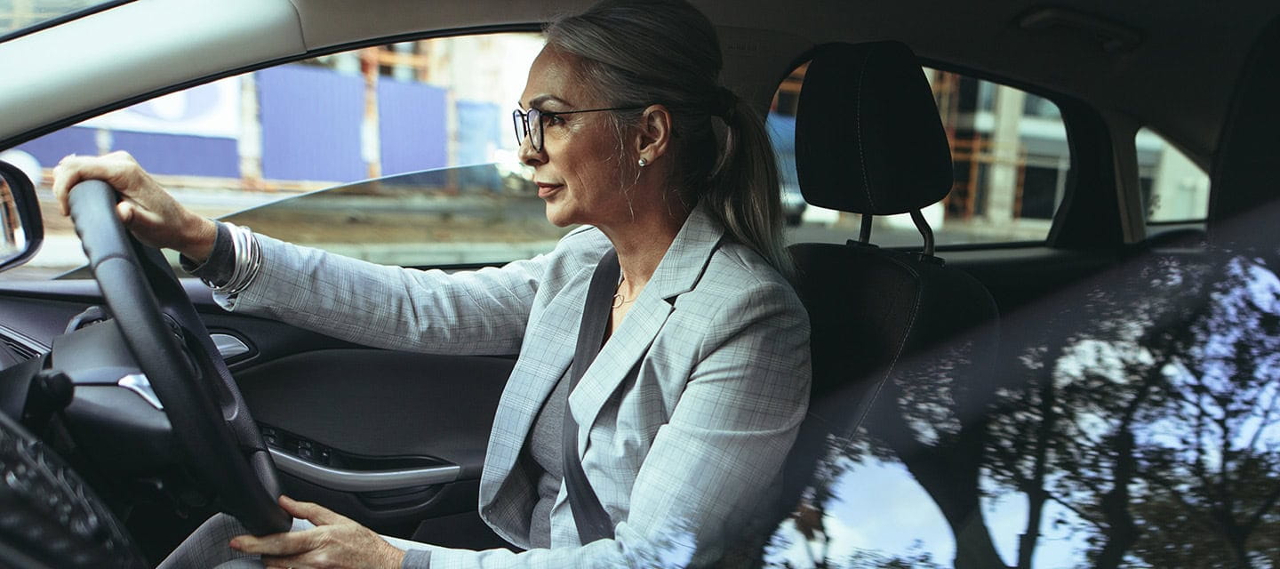 Mature woman in business suit driving a car to office.