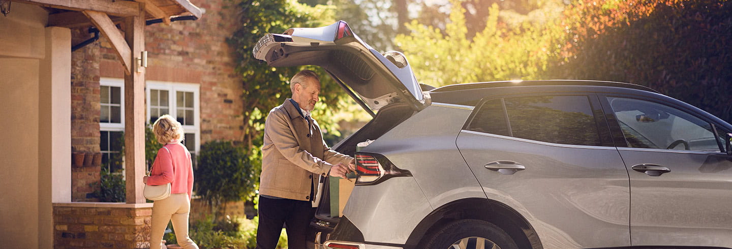 A mature man retrieves bags of shopping from the boot of his car on his driveway