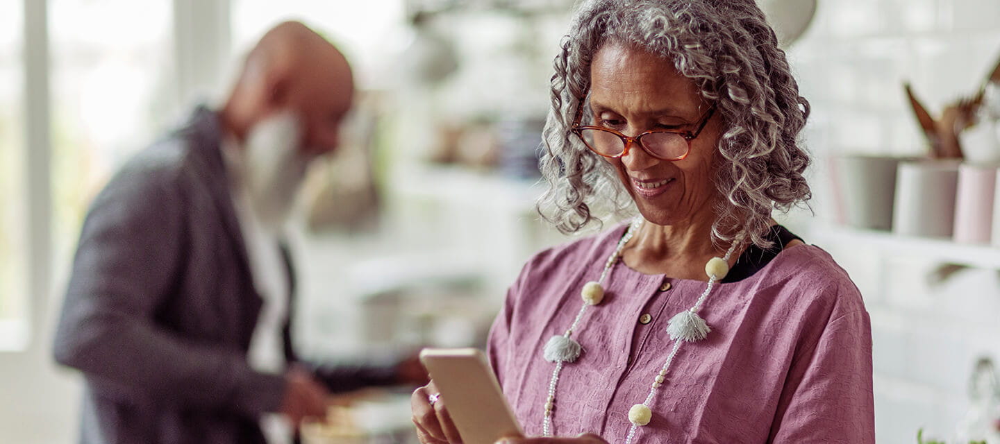 Mature woman in eyeglasses using smart phone in domestic kitchen