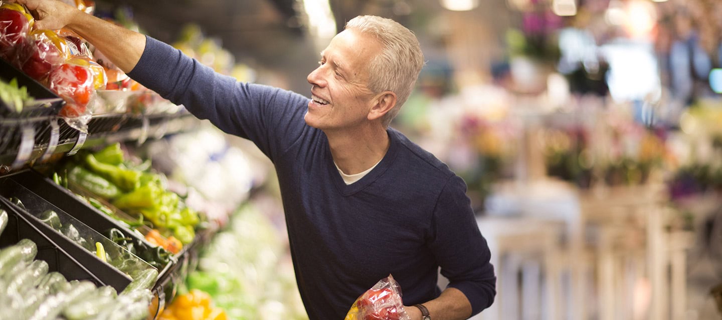 Mature man selects fresh vegetables in the produce section of a supermarket.
