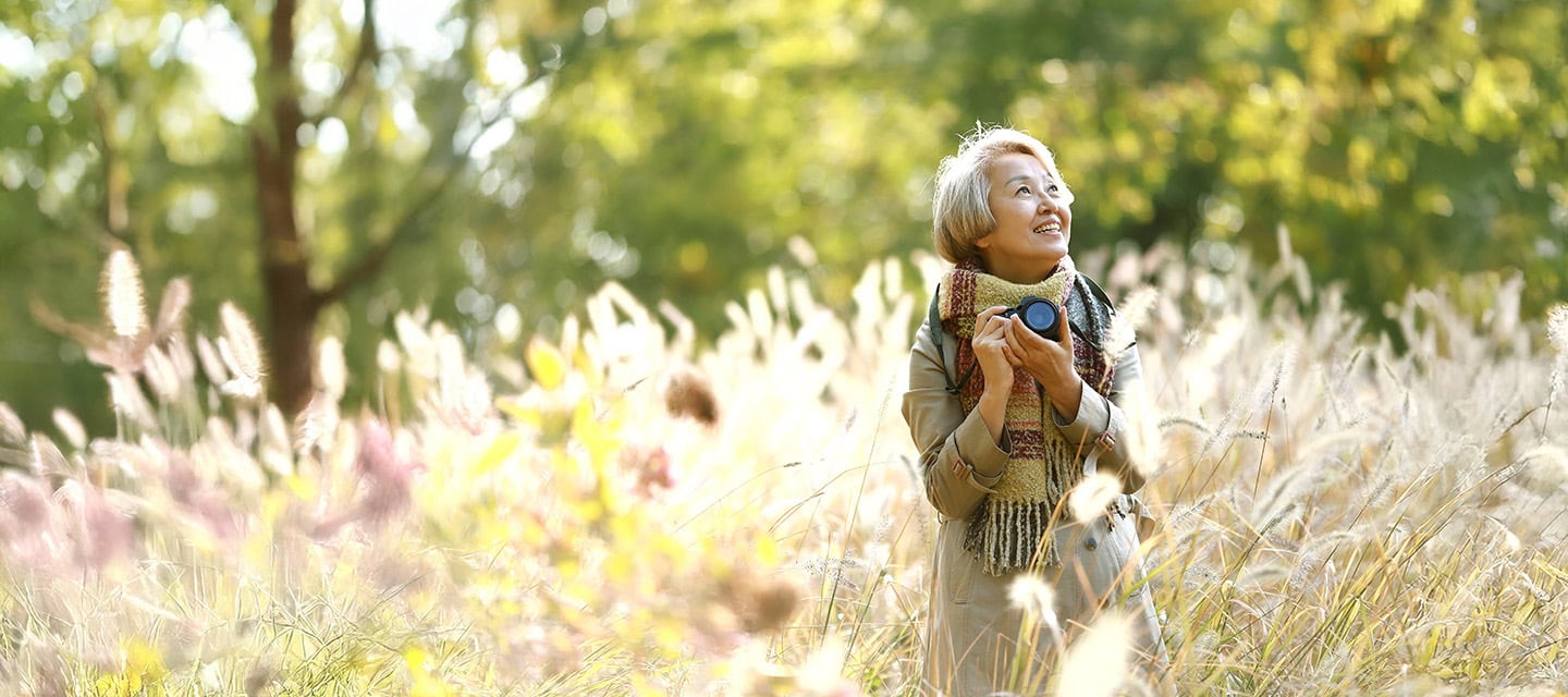 Mature woman taking pictures with camera in autumn park.