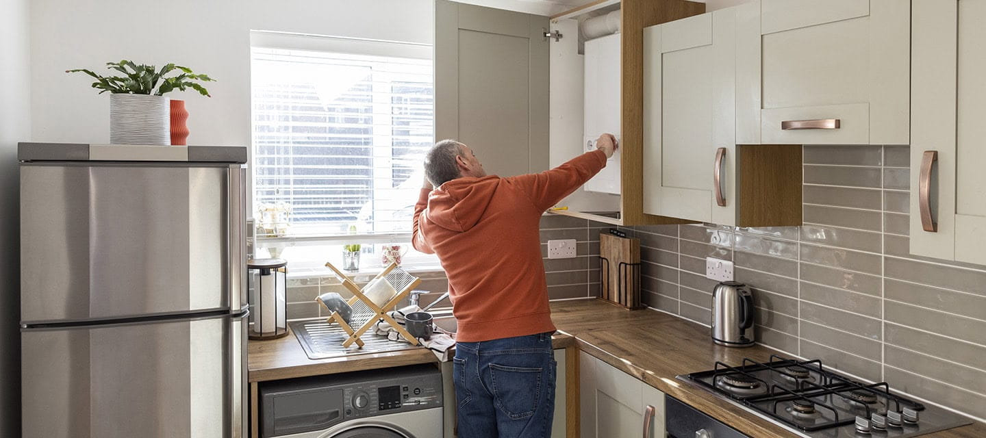 A man in his kitchen adjusting the dials on his combi boiler.