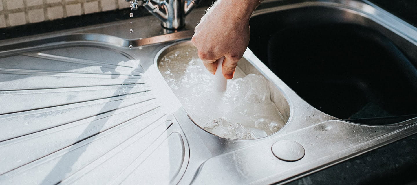 Man plunging a blocked kitchen sink with a manual suction plunger.