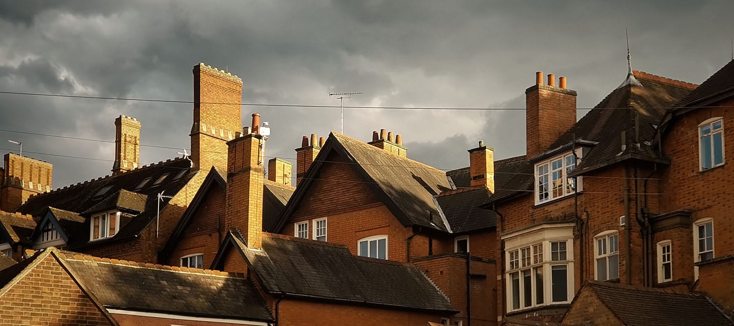 Pitched roofs and chimneys of traditional brick houses in England underneath dark storm clouds