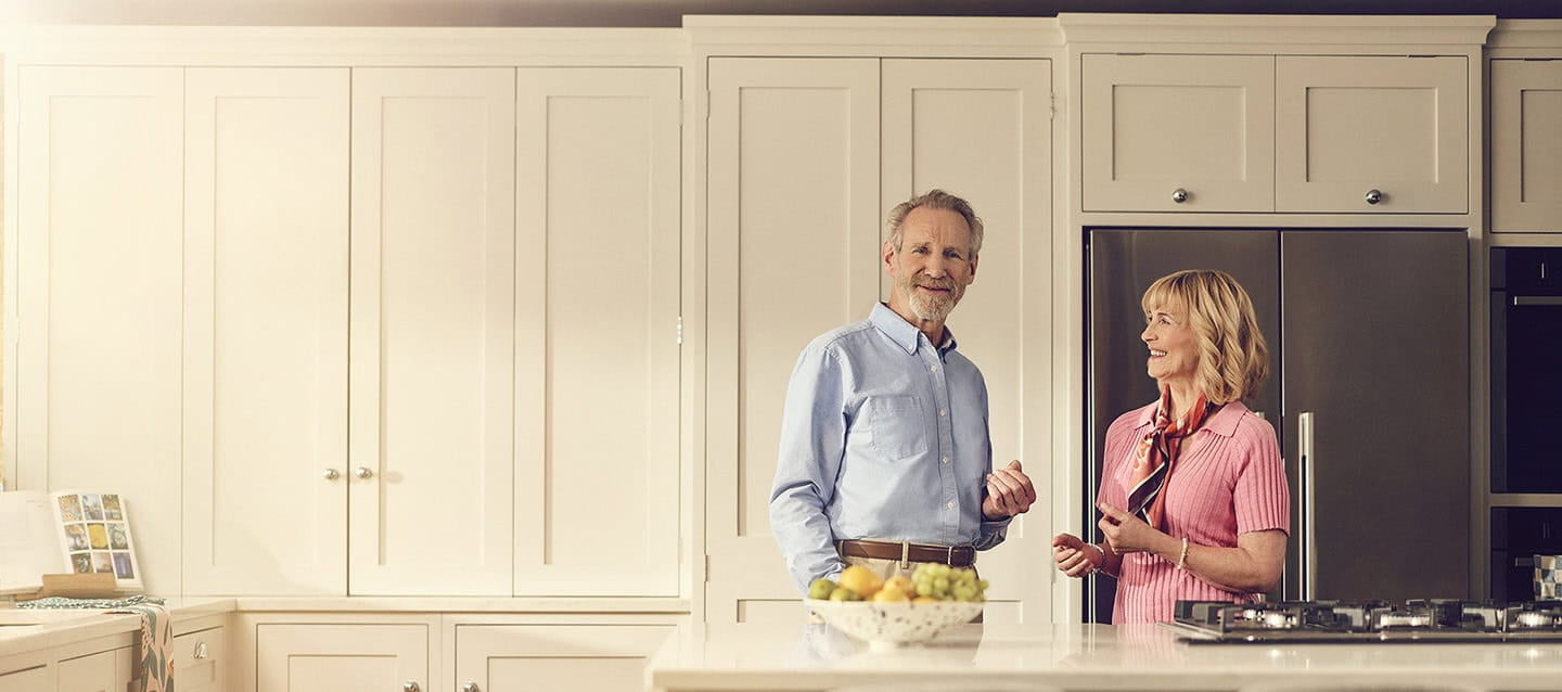 A happy mature couple stood in their kitchen smiling.