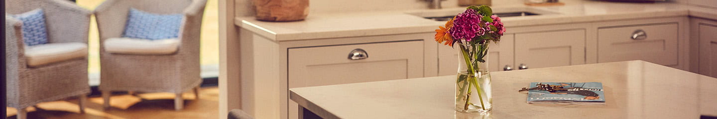 A close up shot of a vase containing flowers stood on a kitchen island