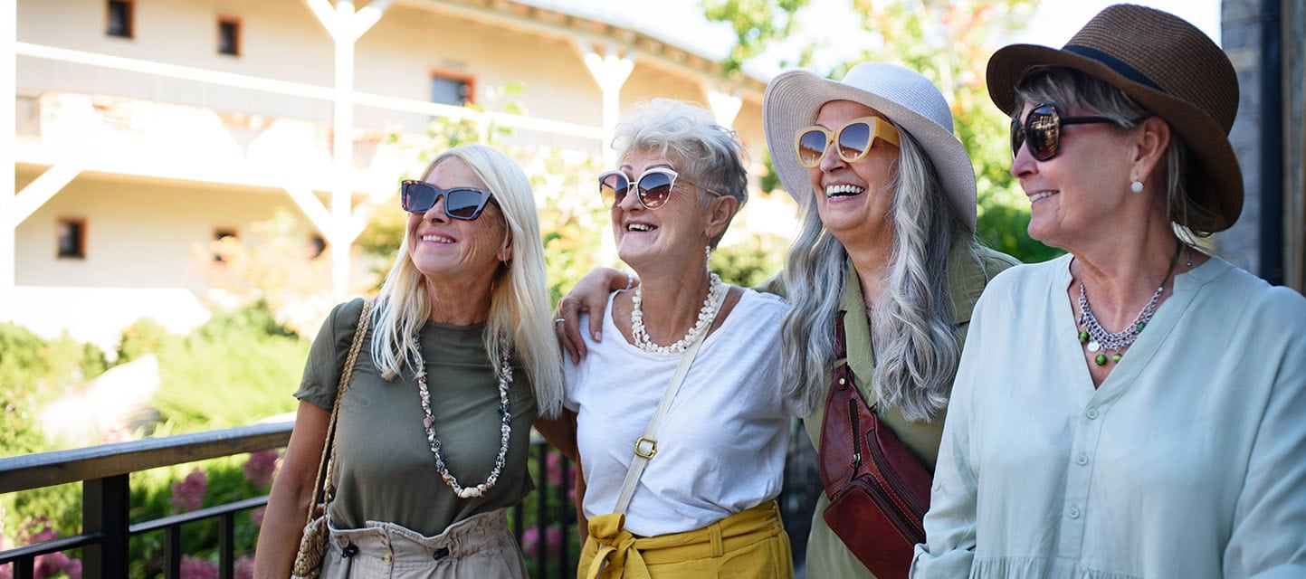 Group of senior female friends standing outdoors on hotel terrace arriving for summer holiday.