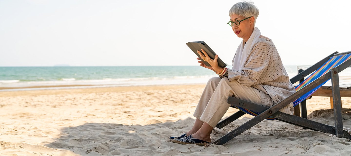 Modern senior businesswoman working on digital tablet with internet at tropical beach in sunny day.