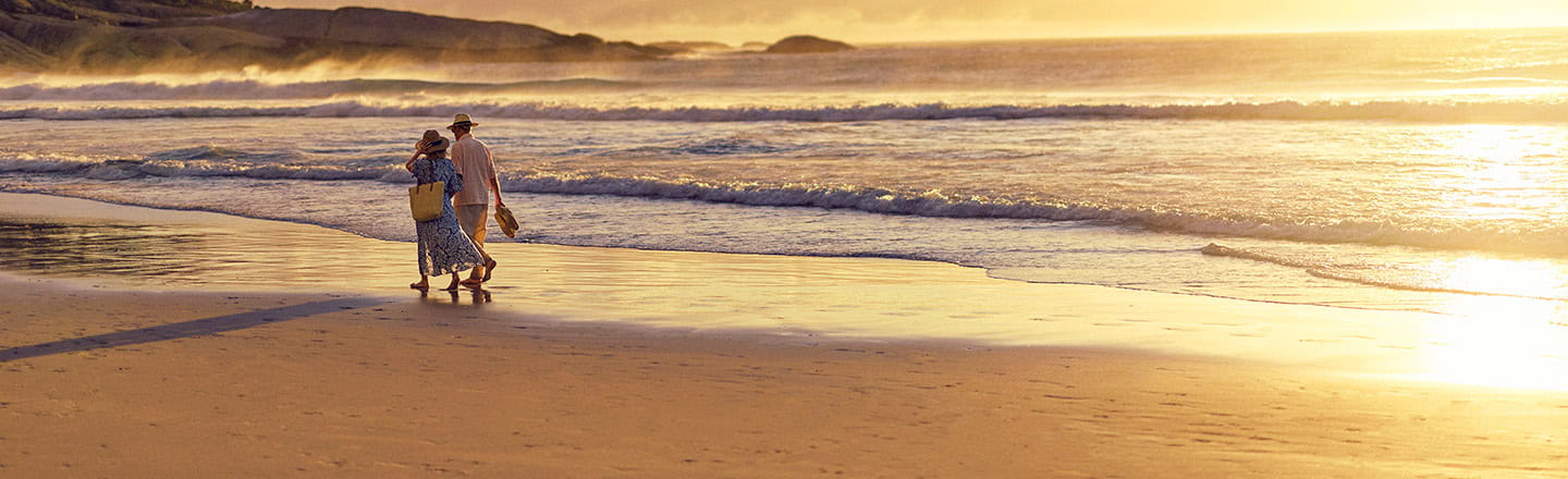 A mature couple walking along a sandy beach as the sun sets