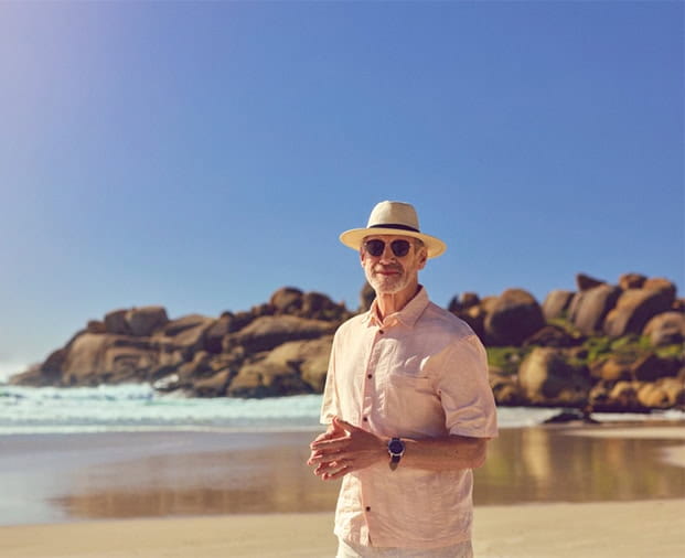 A senior man stood on a sandy beach on a beautiful sunny day.