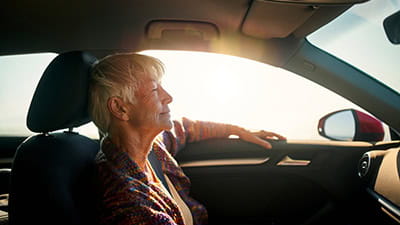 A mature woman sitting in her car on a very sunny day