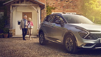 A mature couple walking arm in arm to their car parked on the driveway of their home
