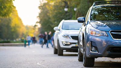 Two cars parked on the road near a row of trees at sunset
