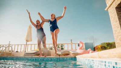 Two mature women jumping in to a swimming pool on a beautiful sunny day