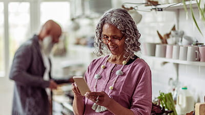 Mature woman in eyeglasses using smart phone in domestic kitchen
