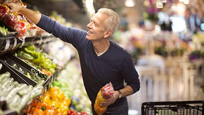 Mature man selects fresh vegetables in the produce section of a supermarket.
