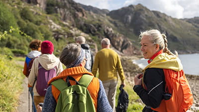 A group of mature and senior friends walking along a footpath near the village of Diabaig on the side of Loch Torridon in the west highlands of Scotland
