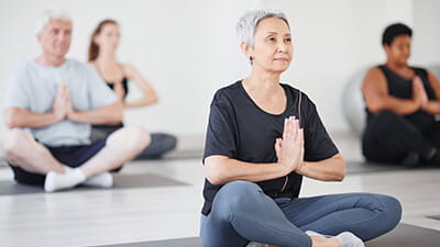 Healthy mature woman sitting on exercise mat in lotus position and doing yoga in the class