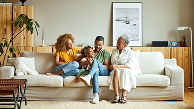 A multi-generational family sat close together on their sofa at home