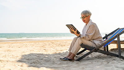Modern senior businesswoman working on digital tablet with internet at tropical beach in sunny day.