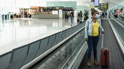 Senior woman using moving walkway inside terminal airport with face mask