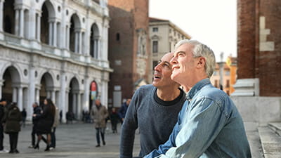 Two men sitting on steps of a historic building and looking up at the architecture