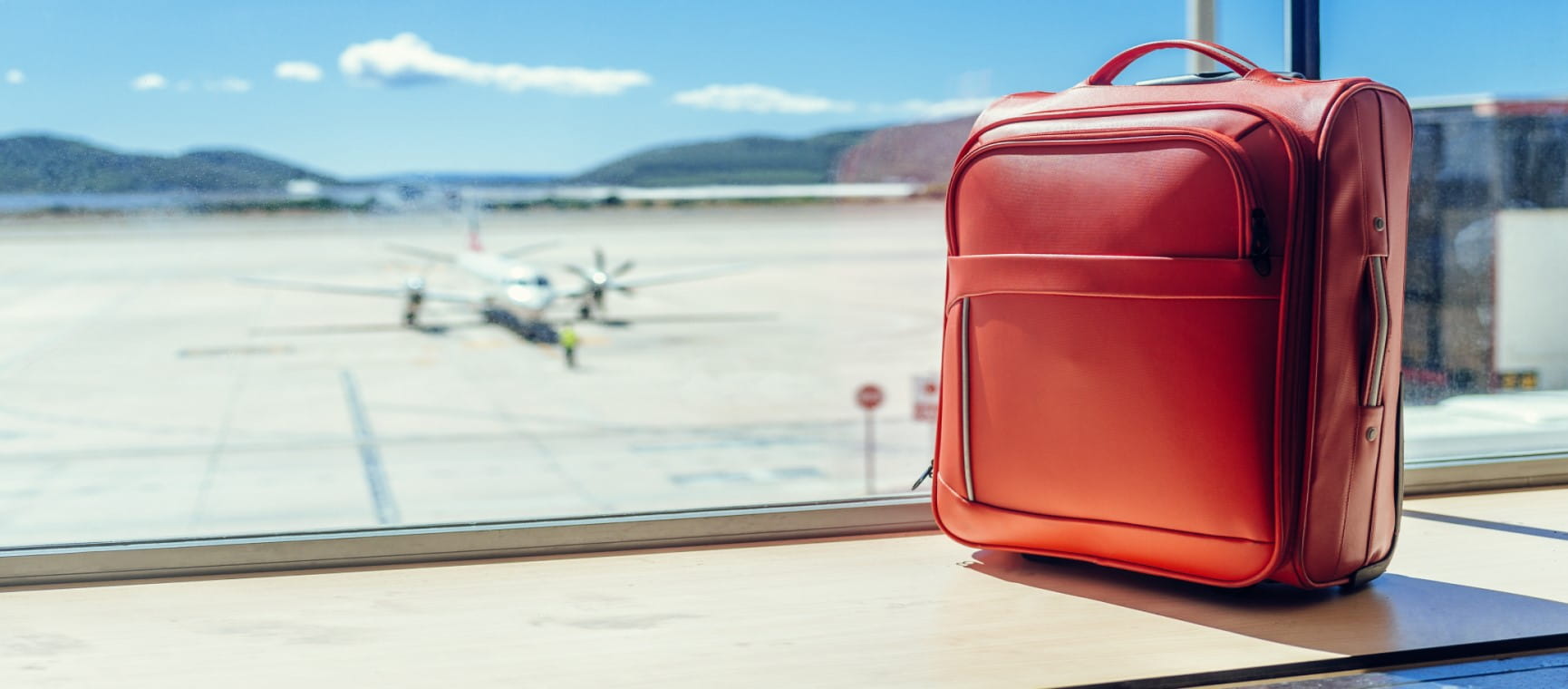 A suitcase with a plane on the runway in the background