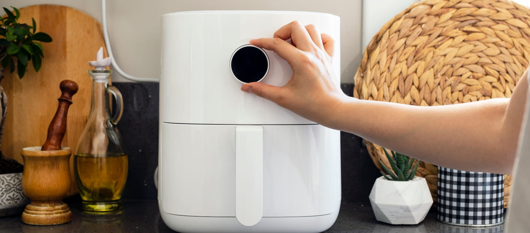 Close-up of a modern white air fryer on a kitchen counter with a hand turning the dial on the front